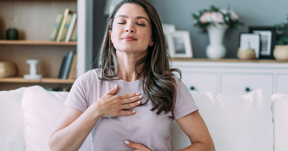 femme brune avec des checeux longs avec un polo faisant un exercice de respiration avec les mains sur le torse