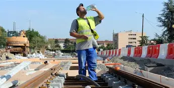 ouvrier avec un gilet jaune, un casque travaillant au soleil avec la chaleur en train de boire une bouteille d'au