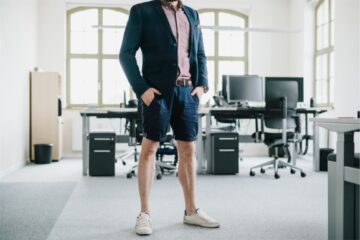 homme en chemise avec une veste bleue en short et mocassin devant son bureau