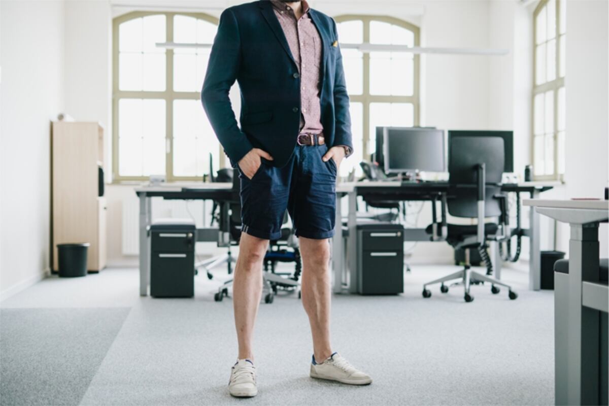 homme en chemise avec une veste bleue en short et mocassin devant son bureau