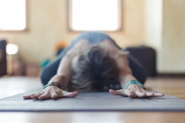 Personne en posture de détente type Balasana, les bras étirés vers l’avant sur un tapis de yoga, dans une ambiance calme.