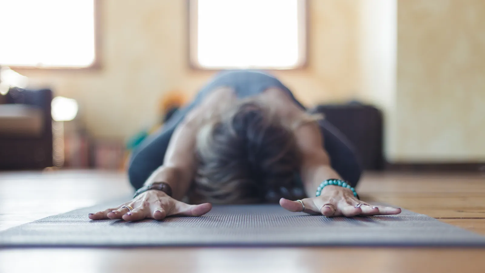 Personne en posture de détente type Balasana, les bras étirés vers l’avant sur un tapis de yoga, dans une ambiance calme.