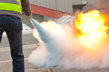 Personne en gilet jaune utilisant un extincteur pour éteindre un feu lors d’une formation incendie en entreprise.