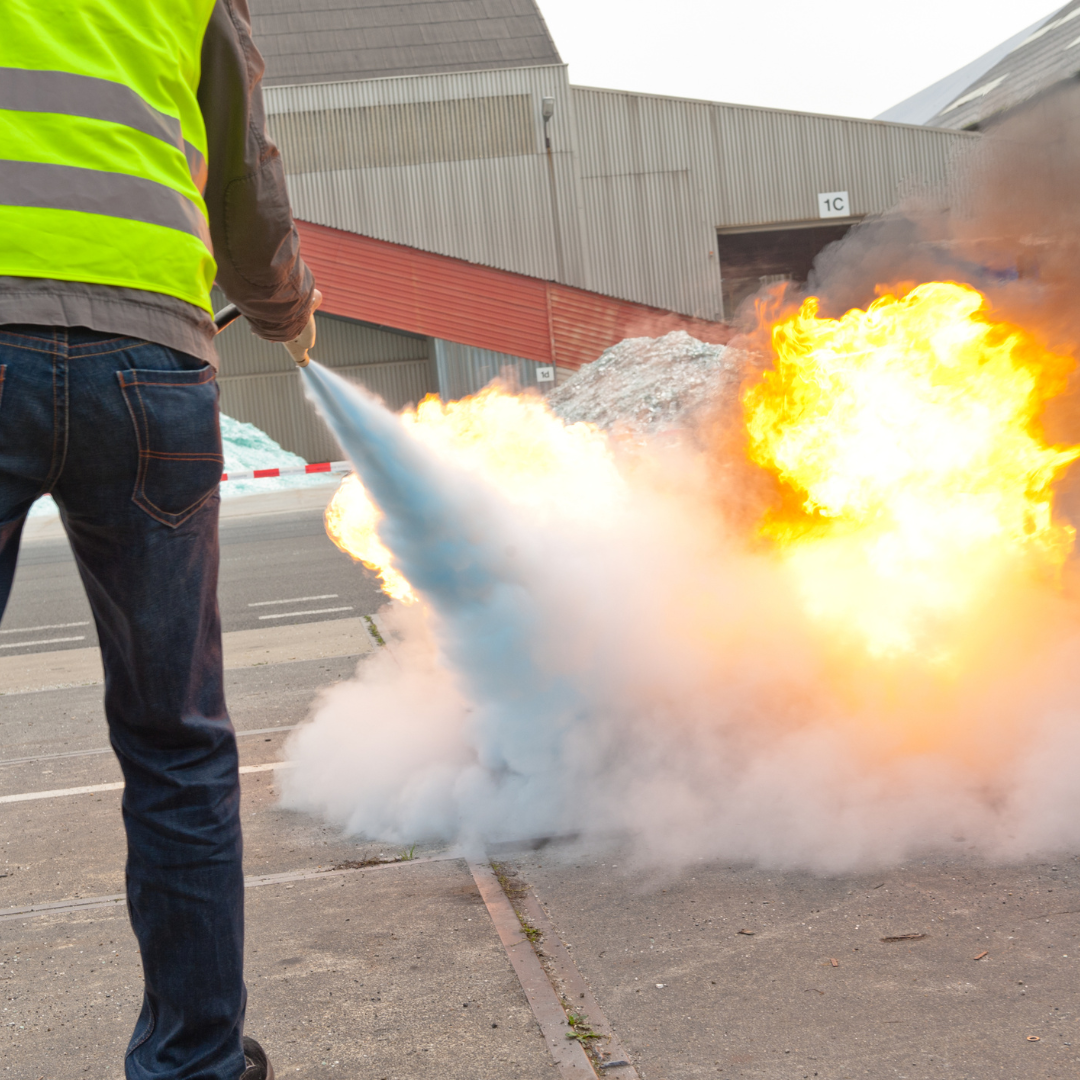 Personne en gilet jaune utilisant un extincteur pour éteindre un feu lors d’une formation incendie en entreprise.